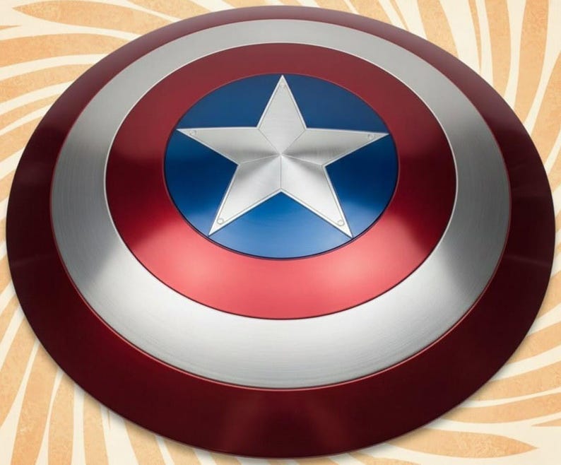 K&ouml;nnte beinhalten: Ein runder Schild in Rot, Silber und Blau. Er hat einen zentralen blauen Kreis mit einem wei&szlig;en Stern, umgeben von silbernen und roten Ringen. Dieser Schild ist eine Nachbildung von Captain Americas Schild.