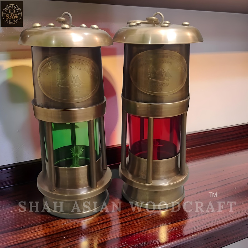 Op de afbeelding: Twee antieke messing lantaarns met gekleurde glazen panelen. E&eacute;n heeft groen glas, de andere rood. Elke lantaarn heeft een gewelfde bovenkant en een basis, met een ovaal embleem. De tekst "SHAH ASIAN WOODCRAFT" staat onderaan.