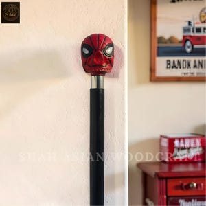 May include: A decorative walking cane featuring a red and black Spider-Man mask design at the top. The cane has a black shaft with a silver metal collar. The cane is a unique collectible item.