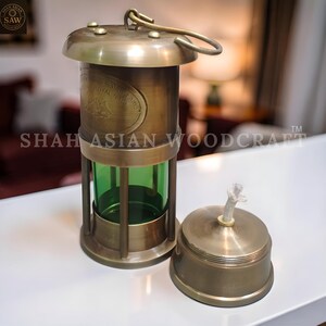 Op de afbeelding: Een vintage messing olielamp met een groene glazen cilinder en een afneembare bovenkant. De lamp heeft een handvat en is gemarkeerd met "Royal Navy". De lamp is ontworpen voor verlichting en decoratieve doeleinden.