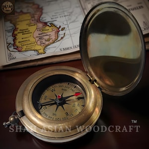 May include: A vintage brass compass with an open lid, displaying a detailed compass rose and a red directional arrow. The compass is set against a backdrop of an antique map. The compass is a classic navigational tool.