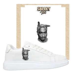 Peut inclure: Baskets blanches avec une image en noir et blanc d'une personne sur le côté. Les baskets ont une semelle blanche épaisse et des lacets blancs. L'image comprend également le texte "SNEAKY Tats" dans une police stylisée.