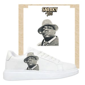 May include: White sneakers featuring a black and white image of a man in a fedora smoking a cigar. The sneakers have a low-profile design with a white sole. The text "SNEAKY Tats" is above the image.