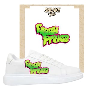 Puede incluir: Zapatillas blancas con suela gruesa, con el texto "Fresh Prince" en verde y rosa. También es visible una pegatina a juego con el mismo diseño. Las zapatillas tienen un diseño limpio y minimalista.