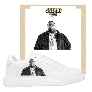 May include: White sneakers featuring a black and white image of a man, with a matching image on a white background. The sneakers have a thick white sole. The text "SNEAKY Tats" is above the image on the background.