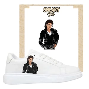 May include: White trainers with a graphic of a person in a black jacket. The trainers have a thick sole and a low-top design. The image also includes a graphic with the text "Sneaky Tats".