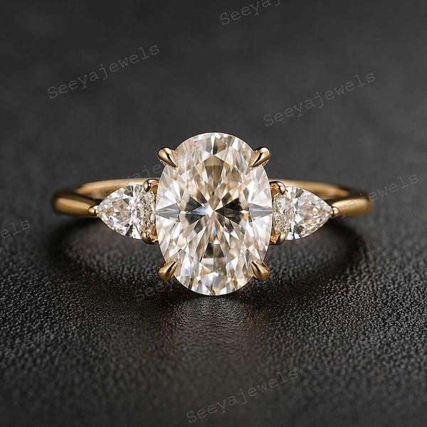 May include: A gold ring with a large oval-cut diamond centre stone, and two smaller pear-shaped diamonds. The ring has a classic three-stone design, set against a dark background. The ring is a piece of jewellery.