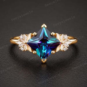 May include: A gold ring featuring a central kite-shaped, iridescent blue and purple gemstone. The band is flanked by two floral motifs, each composed of white petals and small, clear round stones, set on a thin, polished gold metal band.