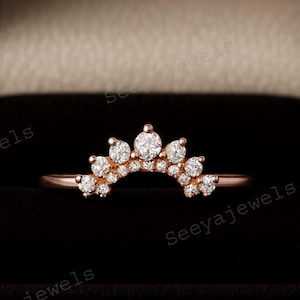 Puede incluir: Un anillo de oro rosa con un diseño curvo, engastado con múltiples piedras preciosas pequeñas y transparentes. El anillo se muestra en un joyero negro abierto, con el nombre de la marca "Seeyajewels" visible en el fondo.