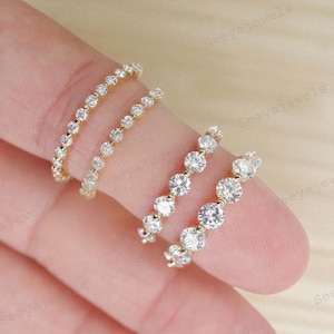 Könnte beinhalten: Vier zarte Goldringe, jeder mit einer Reihe funkelnder, rund geschliffener Diamanten besetzt. Die Ringe werden auf einem Finger präsentiert und zeigen ihr elegantes Design und ihren brillanten Glanz. Der Schmuck ist perfekt für jeden Anlass.