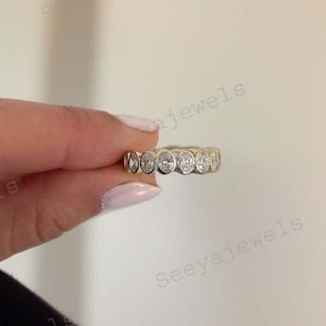 May include: A gold ring with a series of oval-cut, clear gemstones. The ring is displayed against a neutral background, highlighting the sparkle of the stones. The ring is a piece of jewellery.