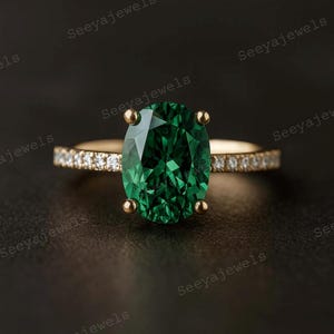 May include: A gold ring featuring a large, oval-cut emerald gemstone. The band is adorned with small, sparkling diamonds. The ring is set against a dark background, highlighting the vibrant green of the emerald.