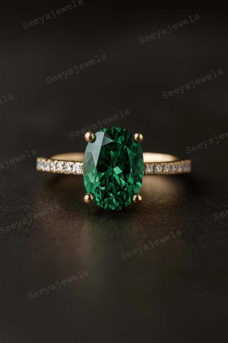 May include: A gold ring featuring a large, oval-cut emerald gemstone. The band is adorned with small, sparkling diamonds. The ring is set against a dark background, highlighting the vibrant green of the emerald.