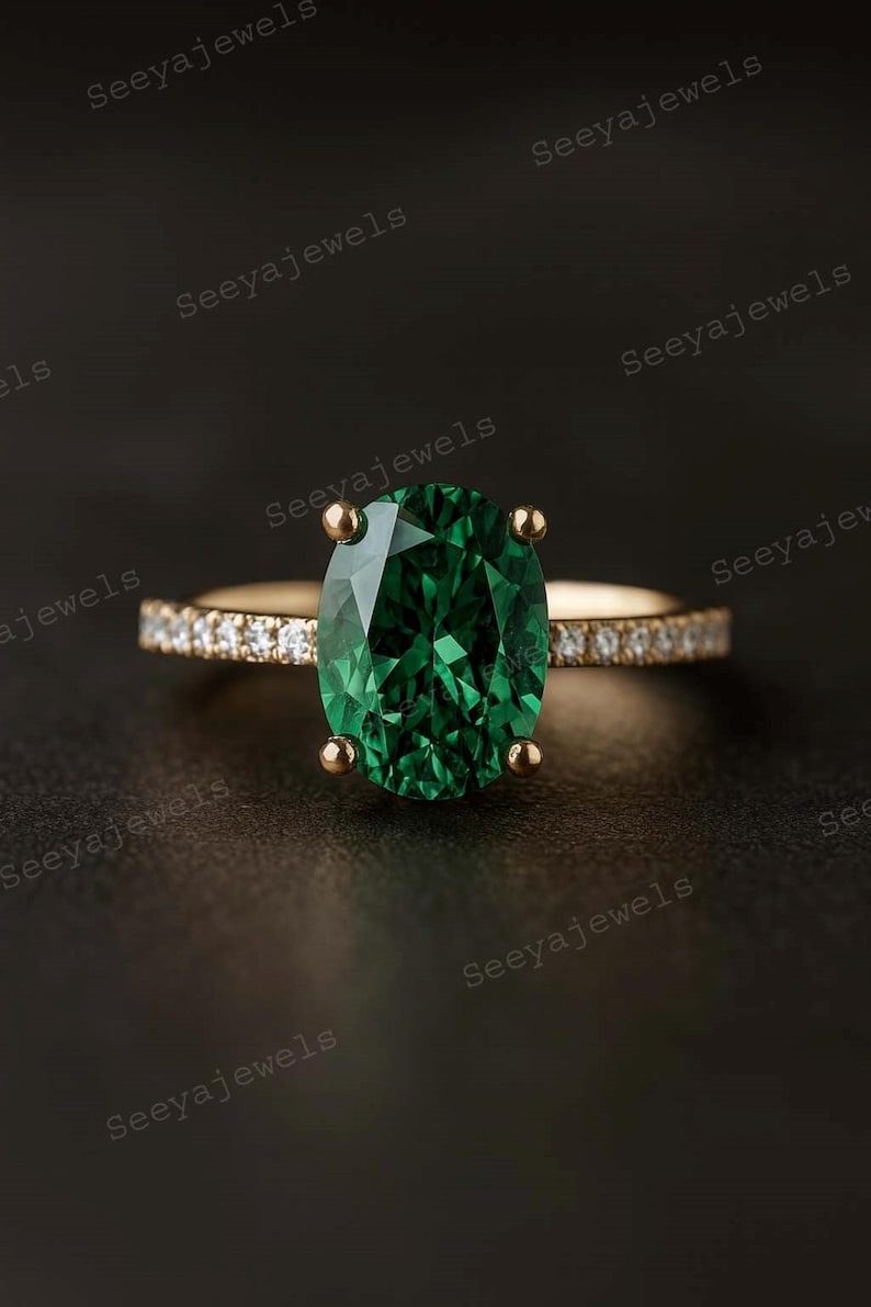 May include: A gold ring with an oval emerald centre stone. The band is embellished with small diamonds. The ring is set against a dark backdrop, accentuating the vivid green of the emerald. The ring is a piece of jewellery.