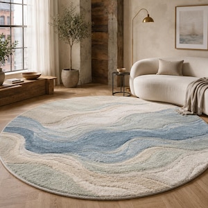 May include: A round area rug featuring a textured, wavy pattern in shades of blue, sage green, cream, and beige. The design consists of flowing, organic lines that create a layered, multi-dimensional appearance across the entire circular surface.