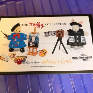 Può includere: Il set di accessori Great Masterpieces della collezione Muffy. Il set include un orso e un coniglio vestiti da artisti, con forniture artistiche in miniatura. L'orso indossa un cappotto blu e il coniglio una giacca nera. Include una fotocamera e un cavalletto in miniatura.