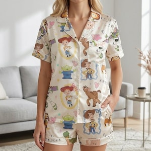Puede incluir: Conjunto de pijama color crema con estampado de personajes de la película de animación Toy Story. El conjunto incluye una camisa de manga corta con botones y pantalones cortos a juego. Los pantalones cortos tienen la palabra "FRIEND" impresa en el dobladillo.