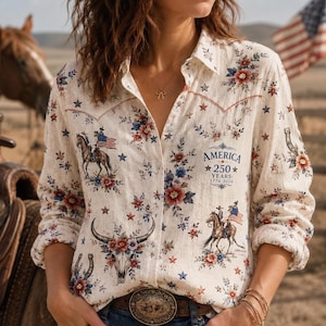 May include: A long-sleeved button-down shirt in cream featuring a repeating pattern of red and blue flowers, stars, horses with riders carrying American flags, and cow skulls. The text AMERICA 250 YEARS 1776 2026 is printed on the chest.