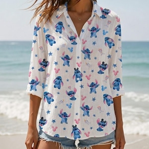 May include: A white button-down shirt featuring a repeating pattern of blue Stitch characters, small pink Mickey Mouse-shaped icons, and blue stars. The shirt has long sleeves with rolled cuffs and a classic collar, crafted from a lightweight fabric.