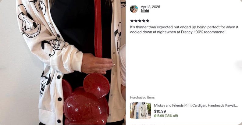 Op de afbeelding: Een wit vest met lange mouwen en een herhalende zwarte lijntekening van stripfiguurgezichten, gedragen over een zwart shirt, gecombineerd met een glanzende rode ronde schoudertas met afgeronde oren en een bijpassende rode riem.