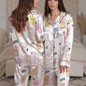 Peut inclure: Ensemble de pyjama en satin blanc avec un motif r&eacute;p&eacute;t&eacute; d'animaux de dessins anim&eacute;s, dont des lapins, des ours et des chiots, avec des &eacute;toiles et des c&oelig;urs. Le pyjama a une bordure noire et les lettres "SKZ" sont imprim&eacute;es.