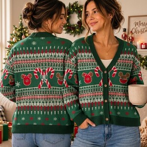 May include: A green V-neck cardigan featuring a festive knit pattern with red and white candy canes, brown mouse-shaped icons, and white snowflakes. The garment has a button-down front, long sleeves, and ribbed cuffs and hem, showcasing a holiday-themed design.