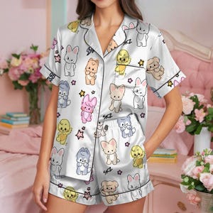 Peut inclure: Ensemble de pyjama en satin blanc avec un motif r&eacute;p&eacute;t&eacute; d'animaux de dessins anim&eacute;s et d'&eacute;toiles. Le haut &agrave; manches courtes et le short ont une bordure noire et les lettres "SKZ" sont imprim&eacute;es sur le short. Un v&ecirc;tement de nuit confortable.