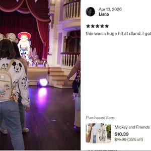 Op de afbeelding: Een wit vest met lange mouwen en een herhalende zwart-witte grafische print van Mickey Mouse en andere tekenfilmfiguren, gedragen over een blauwe spijkerbroek met een kleine beige rugzak, gezien van achteren in een theater.