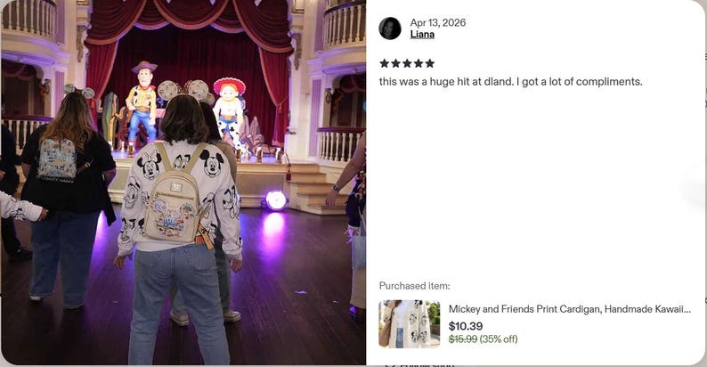 Op de afbeelding: Een wit vest met lange mouwen en een herhalende zwart-witte grafische print van Mickey Mouse en andere tekenfilmfiguren, gedragen over een blauwe spijkerbroek met een kleine beige rugzak, gezien van achteren in een theater.
