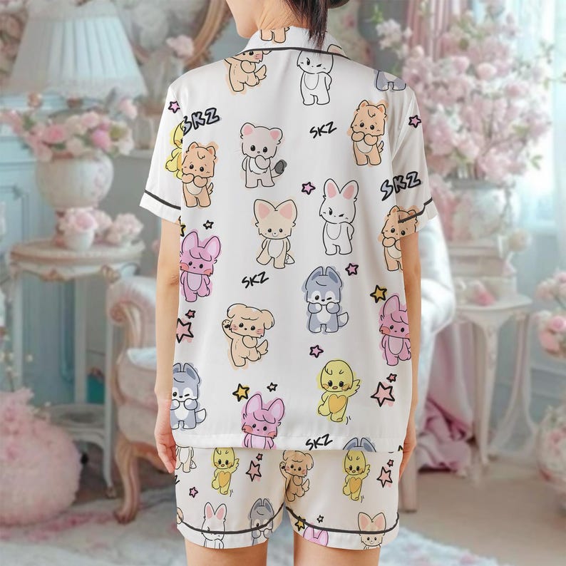 Peut inclure: Ensemble de pyjama blanc avec un motif r&eacute;p&eacute;t&eacute; d'animaux de dessins anim&eacute;s de diff&eacute;rentes couleurs, dont des ours, des lapins et des chiens. L'ensemble pr&eacute;sente une bordure noire et le texte "SKZ". Le haut &agrave; manches courtes et le short cr&eacute;ent un ensemble de v&ecirc;tements de nuit coordonn&eacute;s.