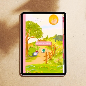 Op de afbeelding: Een digitale tablet toont een fitnessplanner-omslag met een grillige illustratie. Het kunstwerk toont een kikker die een plant water geeft, een zonnig landschap en de tekst "FITNESS PLANNER". Het ontwerp bevat een roze rand en tabbladen.