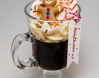 May include: A clear glass mug filled with dark liquid, topped with whipped cream, a gingerbread man, candy canes, and sprinkles. A tag with "Merry Christmas" is attached. Festive holiday theme.