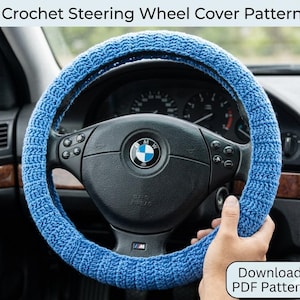 May include: A blue crocheted steering wheel cover on a black steering wheel. The cover is made of a textured yarn and is wrapped around the wheel. The image includes the text "Crochet Steering Wheel Cover Pattern" and "Download PDF Pattern".