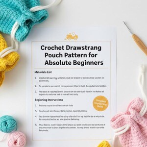 May include: A crochet pattern for a drawstring pouch for beginners. The image shows a pattern sheet, crochet hooks, and several crocheted pouches in yellow, blue, and pink. Yarn balls in pink and teal are also visible.