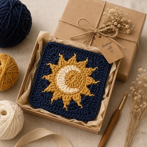 May include: A square crochet motif featuring a yellow sun and white crescent moon design on a dark blue background, presented in a brown cardboard gift box with a tag labeled Handmade with a heart symbol and tied with twine.