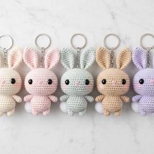 以下が含まれることがあります： パステルカラーの白、ピンク、ミントグリーン、タン、ラベンダーの5つの編みぐるみウサギのキーホルダー。各ウサギは大きな黒い目、ピンクの頬、ふわふわの白い尻尾を持っています。キーホルダーはシルバーのリングに取り付けられています。