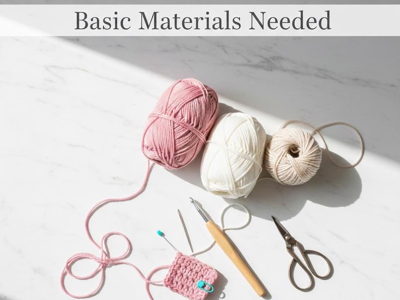 May include: A top-down view shows crochet supplies. Three balls of yarn in pink, white, and beige are alongside a crochet hook, scissors, and a small crocheted square. The text "Basic Materials Needed" is at the top of the image.