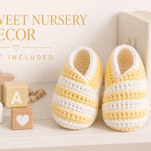 Op de afbeelding: Een paar handgehaakte babyslofjes met horizontale gele en witte strepen. De tekst SWEET NURSERY DECOR en PDF INCLUDED is zichtbaar in de linkerbovenhoek. De slofjes staan naast houten blokken en boeken op een plank.