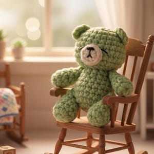Könnte beinhalten: Ein handgefertigter grüner Häkelteddybär sitzt in einem kleinen Schaukelstuhl aus Holz. Der Bär hat eine hellbraune Nase und geschlossene Augen. Der Stuhl ist aus hellbraunem Holz. Ein kleiner Schaukelstuhl aus Holz und ein Fenster befinden sich im Hintergrund.