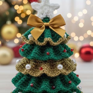 Pode incluir: Uma árvore de Natal de crochê feita à mão, com uma estrela branca e um laço dourado. A árvore é verde com bordas douradas, adornada com pérolas brancas e contas vermelhas. Uma decoração festiva.