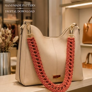 Peut inclure: Un sac à main en cuir beige doté d'une bandoulière amovible en crochet épais de couleur rouille avec un motif ajouré répétitif. Le sac présente des clips en métal doré et une petite plaque rectangulaire dorée. Texte : HANDMADE PATTERN DIGITAL DOWNLOAD.