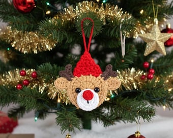May include: A handmade crochet Christmas ornament shaped like a reindeer head. The reindeer has a tan face, brown antlers, a red nose, and a red hat. The ornament is hanging on a Christmas tree with other ornaments.