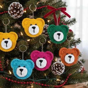 May include: A selection of colourful crocheted bear ornaments, including yellow, green, blue, pink, and orange, adorn a Christmas tree. Each bear features a white face and black nose, with a silver keychain.