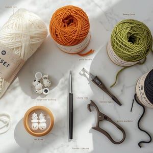 May include: An assortment of craft supplies for knitting and crochet. Includes cream-colored yarn with a label, orange, green, and black yarn balls, a crochet hook, stitch markers, safety eyes, and other tools.