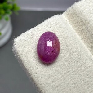 Könnte beinhalten: Ein polierter, oval geformter Edelstein in einem tiefen Magenta- und Rosaton. Der Stein hat einen glatten, abgerundeten Cabochon-Schliff mit einer reflektierenden Oberfläche, die das Licht einfängt und natürliche interne Variationen zeigt.