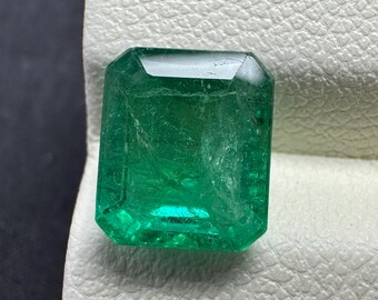 Puede incluir: Una vibrante piedra preciosa de esmeralda con talla esmeralda. La gema es de un color verde intenso y rico con inclusiones internas visibles. La forma rectangular tiene bordes biselados, que reflejan la luz. Esta piedra preciosa es un hermoso ejemplo de esmeraldas naturales.