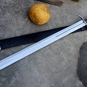 May include: A long, silver sword with a brown handle and a black sheath. The sword has a wide blade and a crossguard. The sheath has a gold-colored end. A round, yellow object is next to the sword.