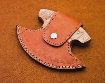 May include: A handcrafted, small cleaver with a wooden handle and a leather sheath. The cleaver's handle is light-colored wood, and the sheath is a warm brown leather with decorative stitching and a snap closure. The cleaver is designed for chopping and cutting.