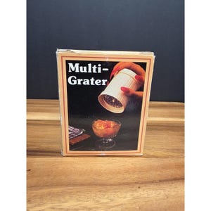 May include: A box for a Multi-Grater with a black background. The box features an image of a grater being used over a glass bowl. The text "Multi-Grater" is displayed in white letters.