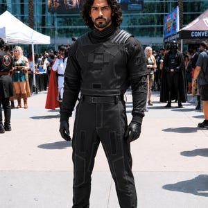 Mandalorian Star Wars Book of Boba Fett inspired 3-piece flight suit cosplay costume featuring a black tactical bounty hunter outfit with flak vest and tailored fit. This Mandalorian suit is crafted with durable fabric, reinforced stitching, and detailed panel design for a screen-inspired look. Ideal for Star Wars cosplay, Comic Con, Halloween, and sci fi events, this outfit offers comfort, mobility, and a bold armor-ready style for dedicated fans.